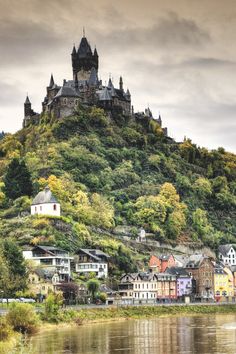 an old castle on top of a hill next to a body of water with buildings below it