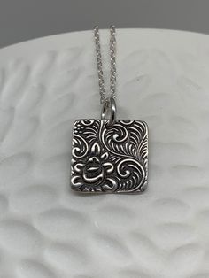 This minimalist tiny rose necklace has been entirely handmade using .999 fine silver. It has been cut out from fine silver precious metal clay, textured, fired and oxidized. The pendant hangs from a sterling silver diamond cut cable chain. This fine silver pendant features an embossed floral rose textured pattern on one side of the pendant and is reversible to a completely different embossed rose pattern on the reverse side. Pendant size: approximately 1/2 x 1/2 inches Chain length: adjustable a Metal Clay Designs, Flower Necklace Silver, Rose Texture, Clay Workshop, Precious Metal Clay Jewelry, Silver Metal Clay, Silver Flower Necklace, Clay Designs, Square Necklace