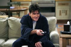 a man sitting on a couch holding a remote control in his hand and smiling at the camera