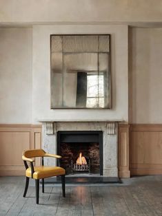 a chair sitting in front of a fire place with a mirror on the wall above it