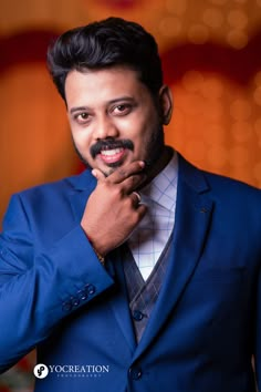 a man in a blue suit and tie posing for the camera with his hand on his chin