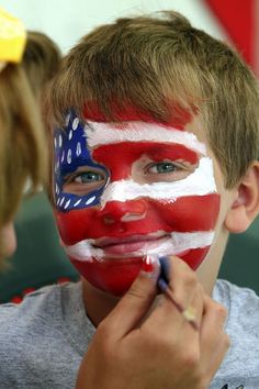 a young boy is getting his face painted with the flag of the united states on it