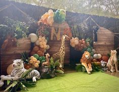 an animal themed birthday party with balloons and jungle animals on the grass, including giraffes