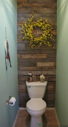 a white toilet sitting inside of a bathroom next to a wooden paneled wall with a wreath on it