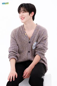 a young man sitting on top of a white bench wearing a sweater and black pants