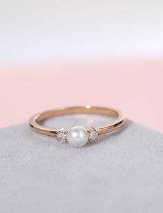 a pearl and diamond ring sitting on top of a white cloth covered surface with a pink background