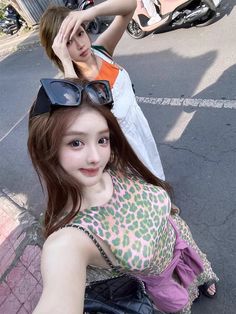 two young women sitting on the ground with one holding her hair up to her head