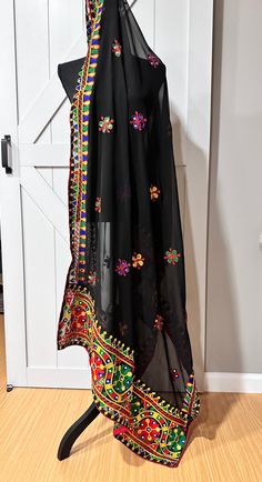 This black Navaratri dupatta features delicate thread work and glimmering mirrors, adding an elegant touch to any outfit. Made from georgette fabric, it is lightweight and comfortable to wear during festive occasions. Enhance your style and make a statement with this beautiful dupatta. Black Chanderi Embroidered Saree Fabric, Unstitched Black Chanderi Embroidered Fabric, Black Sheer Dupatta For Eid, Black Festive Traditional Wear With Sheer Dupatta, Black Semi-stitched Dupatta For Navratri, Black Semi-stitched Dupatta In Traditional Drape, Black Dupatta With Resham Embroidery In Traditional Drape, Black Traditional Wear With Dupatta For Navratri, Black Unstitched Embroidered Fabric In Traditional Drape