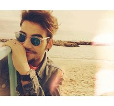 a man wearing sunglasses leaning on a rail at the beach with his hand under his chin