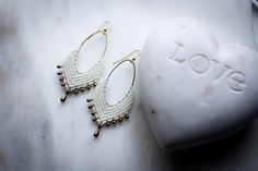 two pairs of white beaded earrings sitting next to a rock with the word love written on it