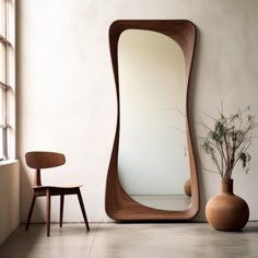 a large wooden mirror sitting next to a vase with a plant in it on top of a hard wood floor