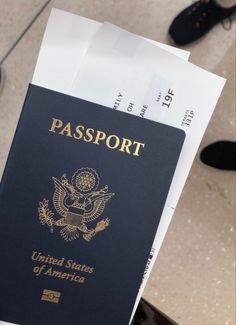 an american passport is held in front of a pair of black shoes on the floor