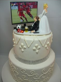 a wedding cake with a couple on top and a tv in the background as well