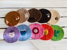 six different colored felt flowers on a white wooden surface