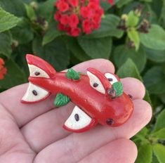 a hand holding a small red toy alligator in it's palm with flowers behind it