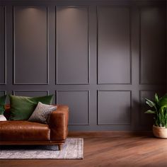 a brown leather couch sitting on top of a wooden floor next to a potted plant