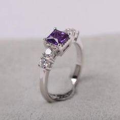 an engagement ring with a purple stone surrounded by three white diamonds on a gray surface