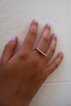 a woman's hand with a gold ring on her left hand, against a white wall