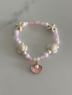 Pink Beach themed bracelet with turtle and starfish beads plus a shell charm with a pearl. Includes an assortment of beautiful light pink beads that looks like a sunset. Elastic band that fits any sized wrist making it perfect for anyone! Bracelet Beach Summer, Cheap Beaded Bracelets With Heart Beads For Beach, Pink Starfish Jewelry For Gift, Summer Themed Bracelets, Coral Round Beads Bracelets For Beach, Coral Round Beaded Bracelets For Beach, Coral Round Beads Bracelet For Beach, Pink Adjustable Strand Jewelry, Handmade Pink Strand Jewelry