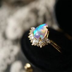 an opal and diamond ring sits on a black stand