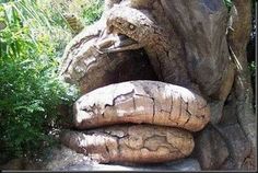 an animal statue made out of wood in the middle of some rocks and plants around it