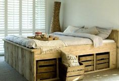 a bed made out of wooden crates with pillows and blankets on it, in a room with white walls