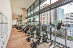 a row of exercise machines in a gym next to a large window with city view