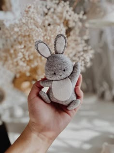 a hand holding a small stuffed animal in front of a vase with flowers on it