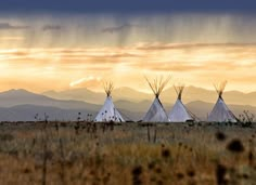 three teepees are in the field with mountains in the background