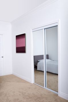 a bedroom with white walls and carpeted flooring has mirrored doors leading to a bed