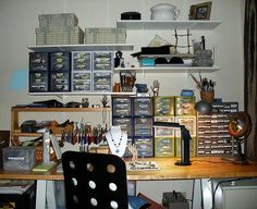 an office with lots of clutter on the desk and shelves above it that are filled with items