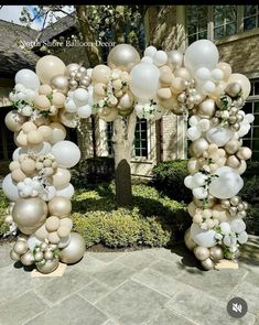 an arch made out of balloons in front of a house with a tree and bushes