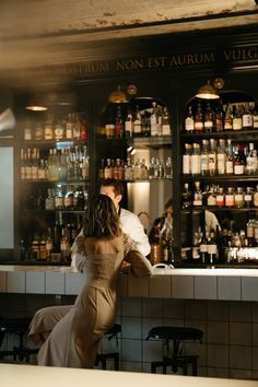 a man and woman sitting at a bar in front of shelves filled with liquor bottles