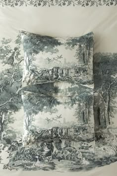 two pillows sitting on top of a bed covered in blue toiler print fabric