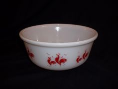 a white bowl with red roosters painted on the side and inside, against a black background