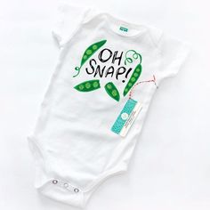 Our quirky and cute "Oh Snap! Peas" baby onesie is made in the USA from 100% organic cotton and features a lapped neckline and 3 metal snaps for easy on/off diaper changes. Makes a fun baby gift for anyone, but is especially cute for vegetarian parents, foodie lovers, or those who enjoy gardening! Available in sizes 0-3M, 3-6M, 6-12M, and 12-18M. hades of green, black and White. Vinyl heat transfer print. Each baby onesie is proudly sewn in the USA and is joyfully printed in small batches by Sun Organic Cotton Onesie For Spring Playtime, Spring Organic Cotton Onesie For Playtime, Spring Playtime Organic Cotton Onesie, Fitted Organic Cotton Onesie For Playtime, Playful Cotton Onesie For First Birthday, Playful Organic Cotton Onesie For Playtime, Fun Cotton Bodysuit For Playtime, Playful Short Sleeve Onesie As A Gift, Playful Cotton Onesie