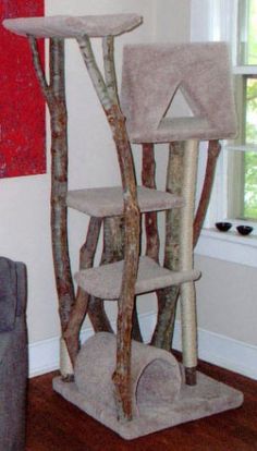 a cat tree in a living room next to a couch and window with red painting on the wall