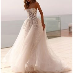 a woman in a wedding dress standing on a balcony next to the ocean with her hand on her hip