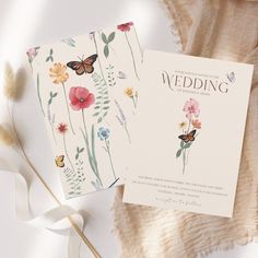 two wedding cards with flowers and butterflies on them, next to a white flower bouquet