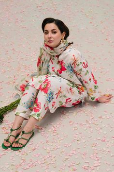 a woman sitting on the floor with flowers all over her body and wearing green flip flops