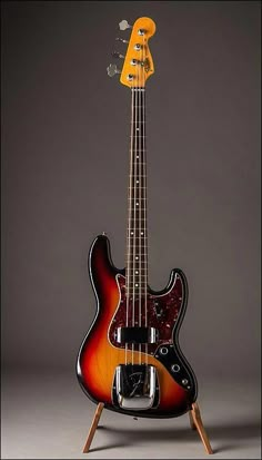 an electric bass guitar sitting on top of a wooden stand in front of a gray background