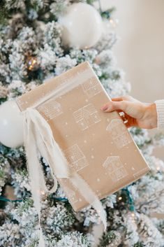 a person holding a brown gift box in front of a christmas tree with white ornaments