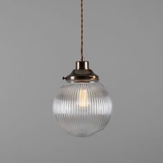 a clear glass light hanging from a metal hook on a gray wall with a brown cord