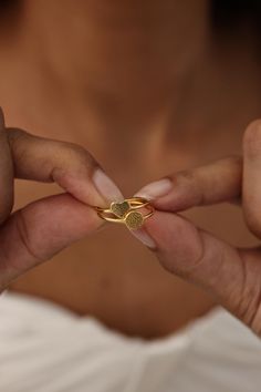 a woman holding onto a gold ring with two hearts on it