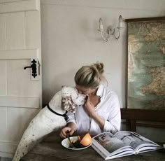 a woman sitting at a table with a dog eating food