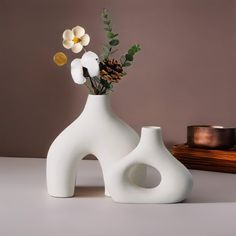 a white vase with flowers in it sitting on a table next to a candle holder