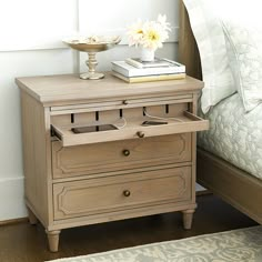 a nightstand with two drawers and a book on top of it next to a bed