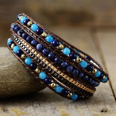 a stack of bracelets sitting on top of a wooden table next to a rock