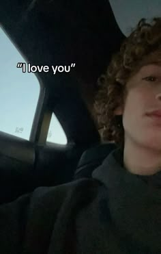 a man with curly hair sitting in the back seat of a car and looking off into the distance