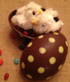 two stuffed animals sitting in a chocolate egg with candy on the ground next to it